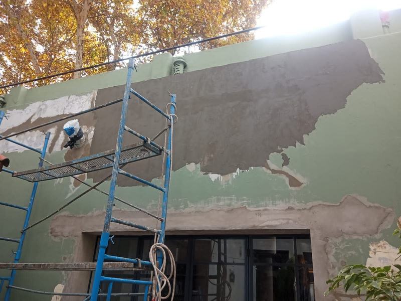 Fachada con andamio y un sector grande de revoque nuevo aplicado sobre la pared.