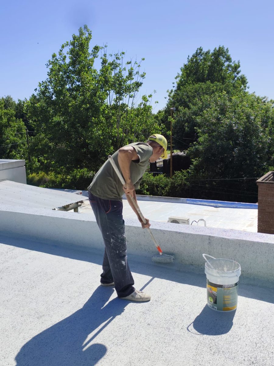 Operario aplicando membrana líquida blanca con rodillo sobre un techo plano.